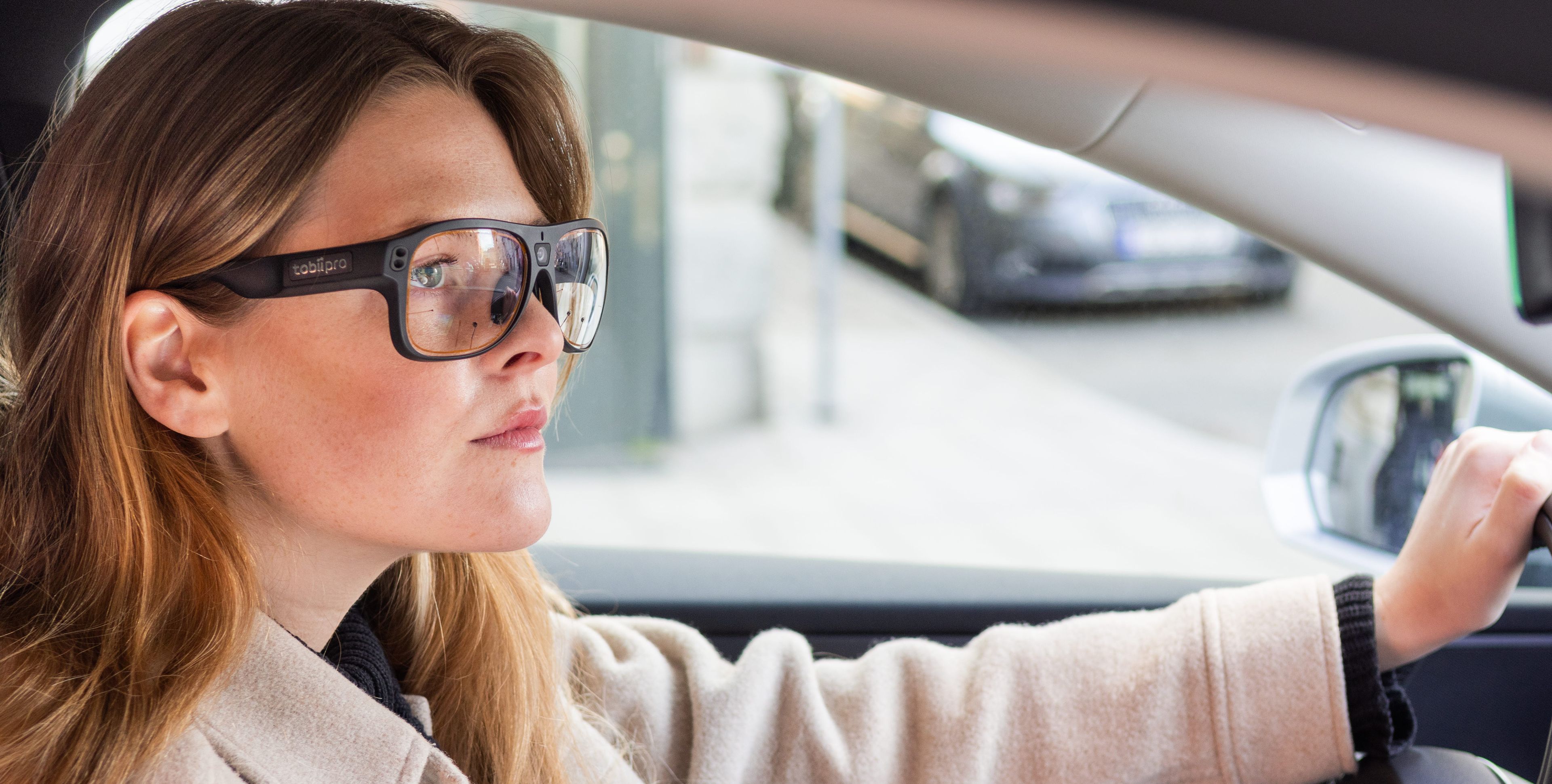 A woman is driving a car wearing Tobii Pro Glasses 3. 