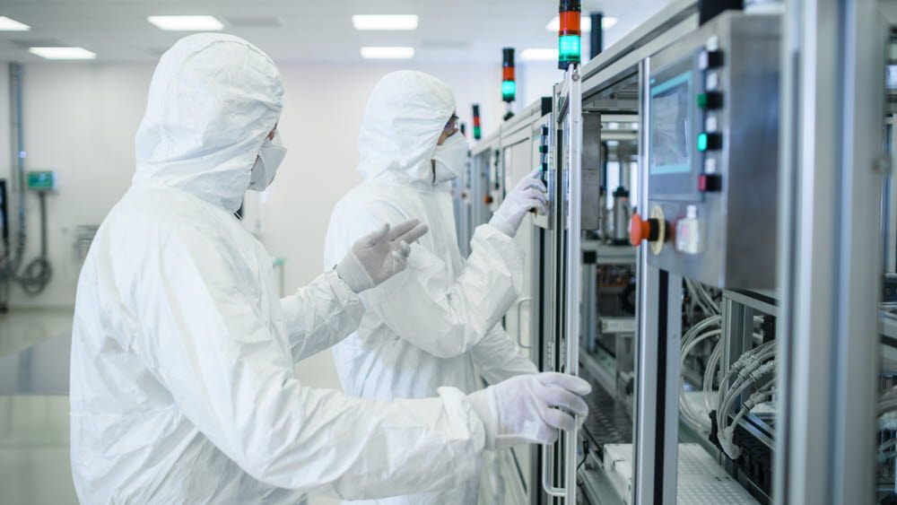 Workers are setting up machines in front of equipment in a sterile room.