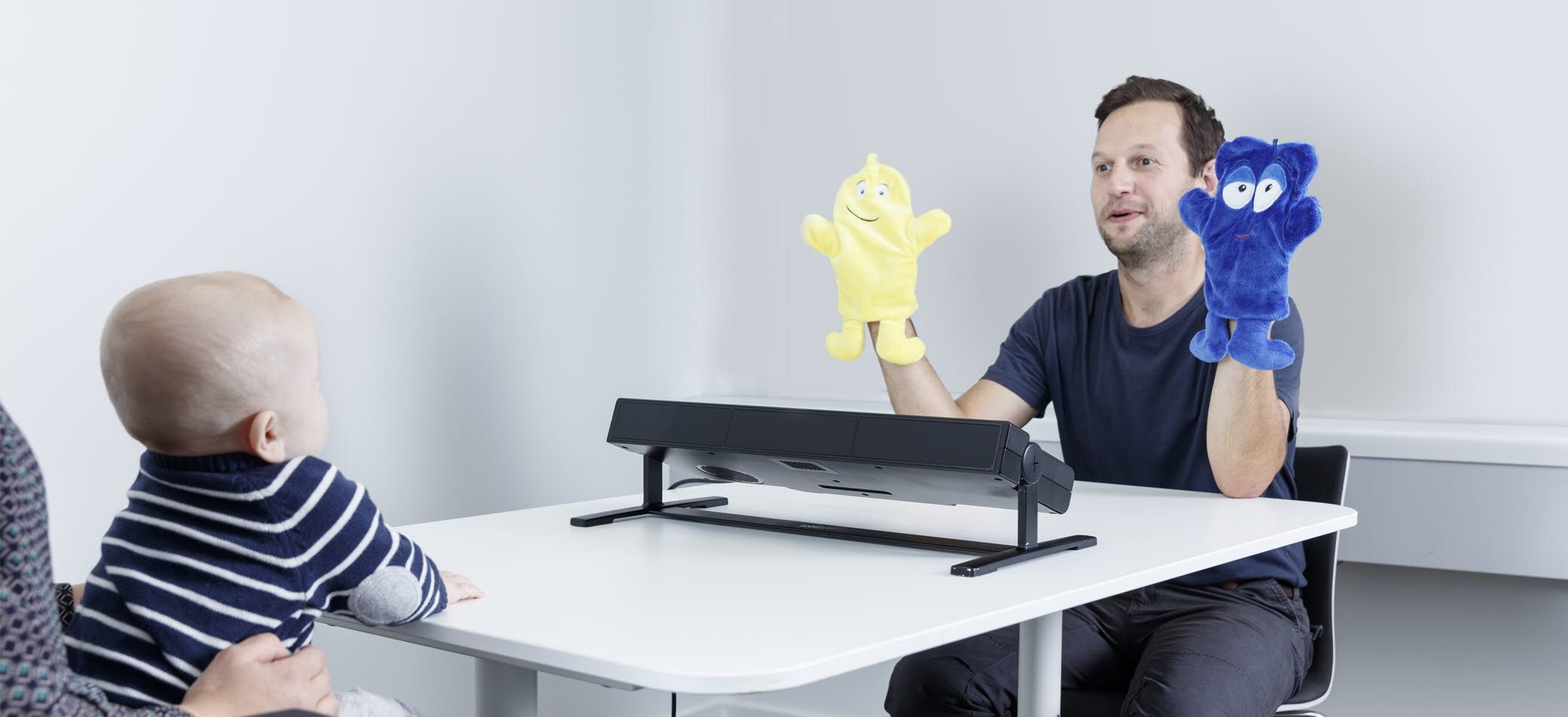An infant in front of Tobii Pro Spectrum eye tracker looks at a researcher with poppets 