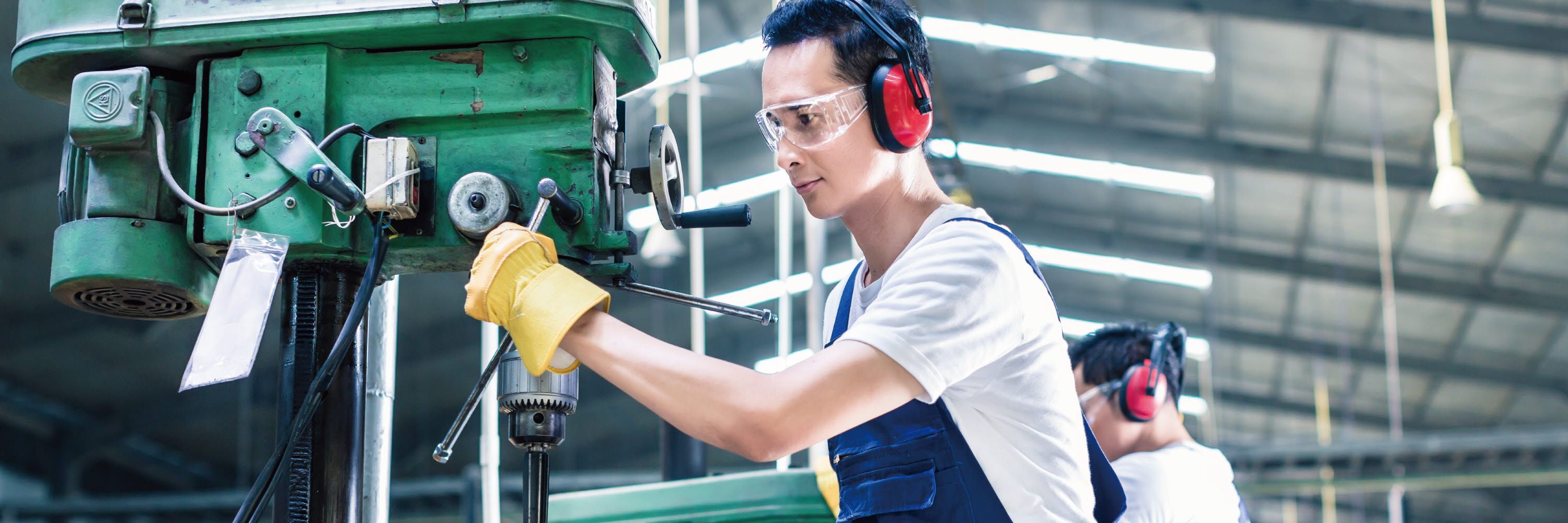 A man is working the machine with protective glasses on.